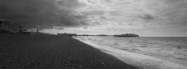 Brighton Pier seen from a few hundred meters away, showing it going from the road into the sea. Over Bright are some stormy looking clouds.