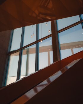 A view from inside a building walled with orange panels, looking up at a window with some light bulbs hanging in front of it.