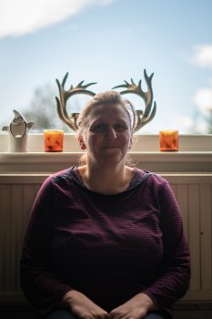 A portrait photo of my sister Karen, showing her sat in front of a window. On the window sill are some antlers, and the photo is angled to make it look like Karen has antlers.