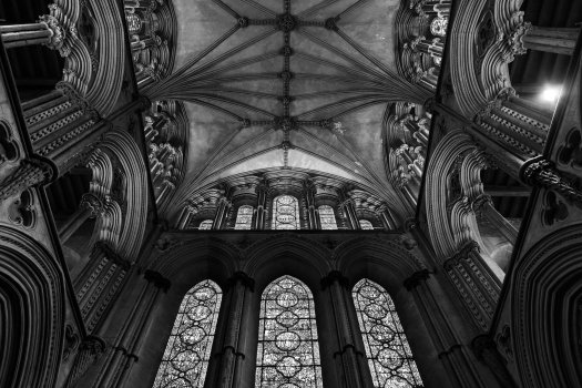 A photo looking up at the ornate celing and end wall of a cathedral, showing lots of detailed stone work and stained glass. The photo is almost, but not quite, symmetric, just out by a degree or so.