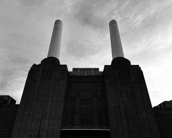 A black and white photo of the front of Battersea Power Station, showing a silhouette of the main brick building and two of the tall chimneys
